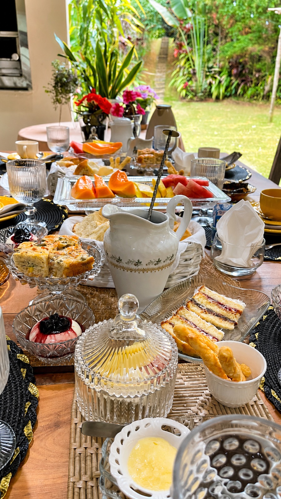 Mesa do café da manhã posta no jardim, com frutas, pães e bolos