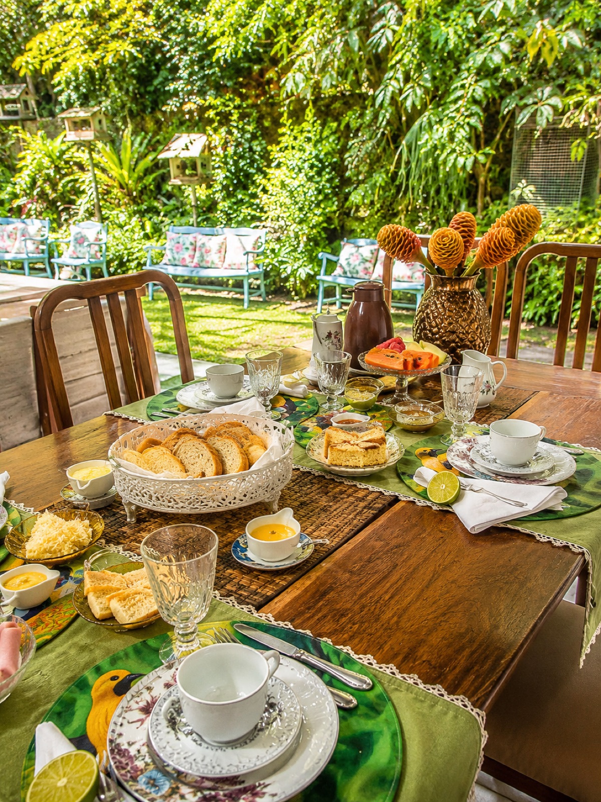 Mesa do café da manhã posta no jardim da pousada, com pães, bolos e frutas