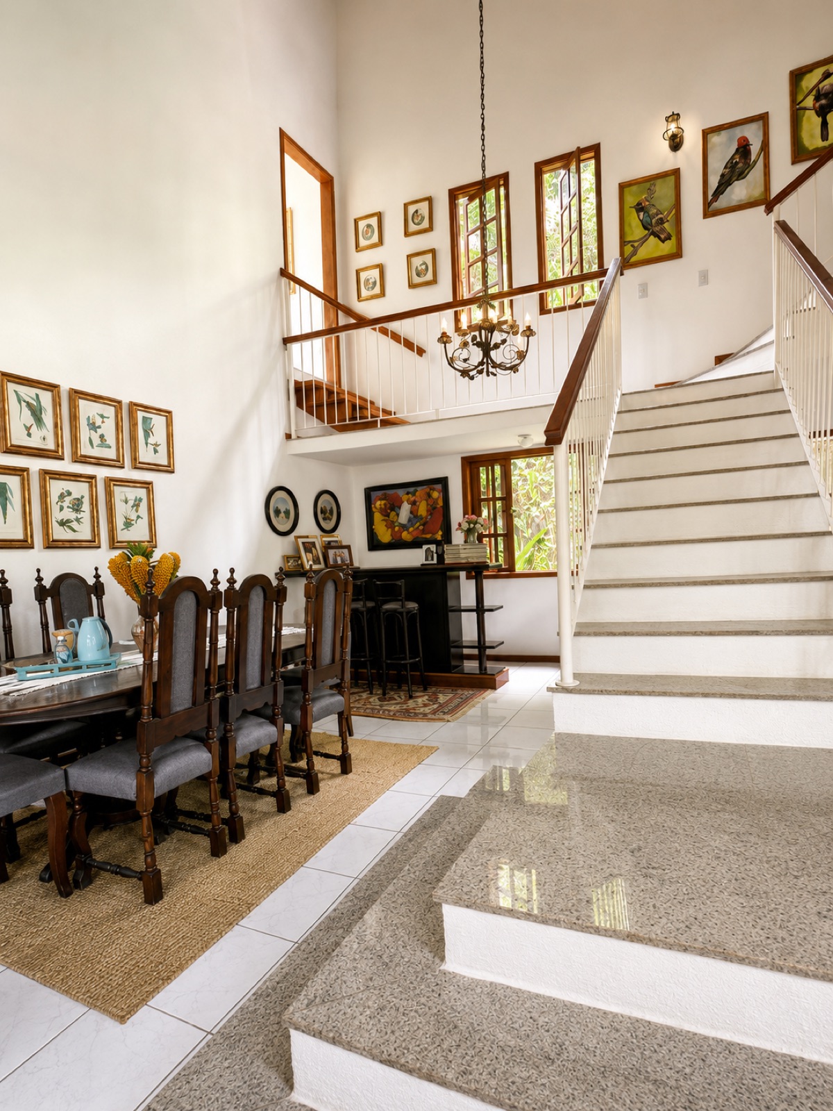 Sala de jantar com mesa de madeira e parede de quadros até o pé-direito alto