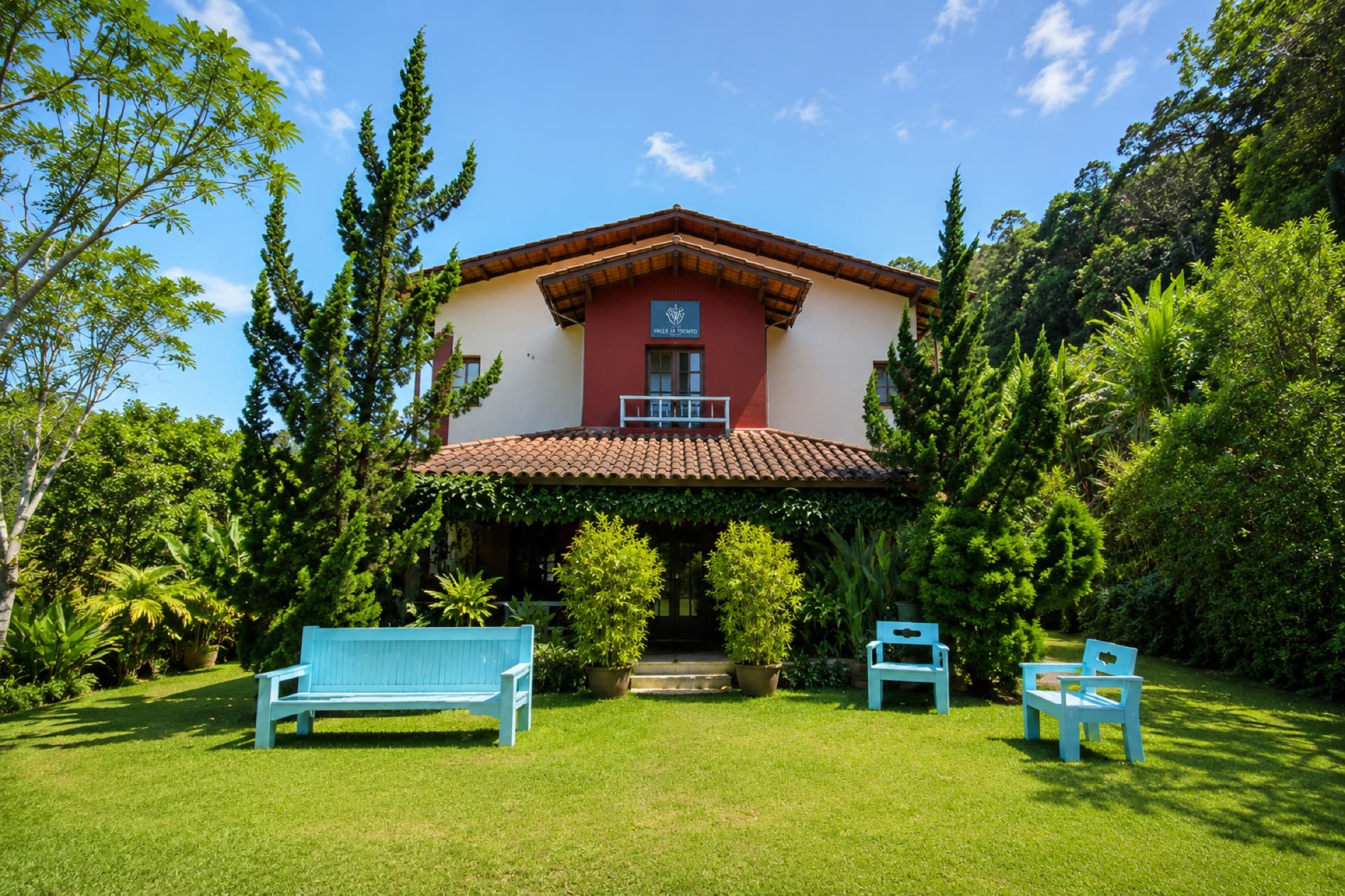 Fachada da Pousada Valle di Trento com jardim e bancos azuis em Santa Teresa, ES